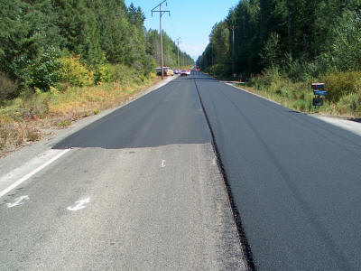 Photo showing the existing pavement (left, front), a leveling course (left rear), and the final surface course (right). In this particular instance, leveling course was only placed periodically where it was needed along the entire 8 mile job.