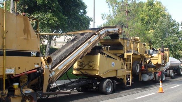 This example CIR equipment train shows a milling machine feeding material into a mobile recycling unit that combines a screening and crushing unit with a pugmill mixer. The paver and compaction equipment are on the right outside of the photo frame. (Photo courtesy of IPMA International Pavement Management Association)